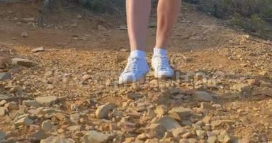 漂亮的女人穿着白色运动鞋，沿着石质的地面前进。 在沙漠里散步。